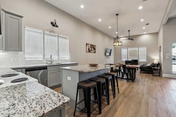 A kitchen with a granite countertop, bar stools, a dining area with a table and chairs, and a ceiling fan.