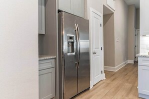 A kitchen with a stainless steel refrigerator, white cabinets, and a wooden floor.