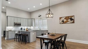 Une cuisine moderne avec des meubles gris, un îlot central doté de tabourets, une table à manger avec des chaises et un luminaire suspendu.