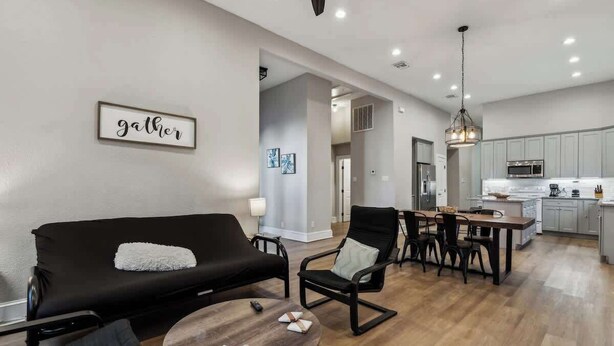 Un salon moderne avec un canapé noir, une table basse ronde en bois et un coin repas comprenant une table et des chaises en bois.