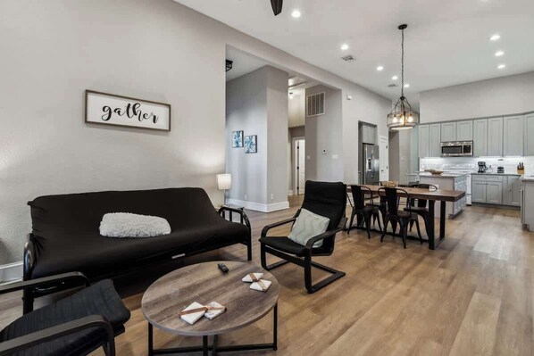 A modern living room with a black sofa, a round wooden coffee table, and a dining area with a wooden table and chairs.