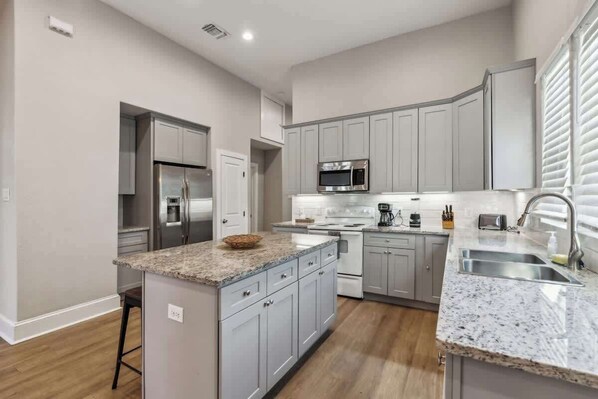 A modern kitchen with grey cabinetry, a granite countertop, stainless steel appliances, and a built-in microwave.