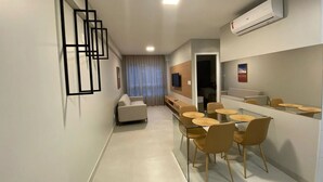 A modern hotel room with a dining area, a sofa, and a TV. - Edifício Promenade II - Apto 403 (Maceio)