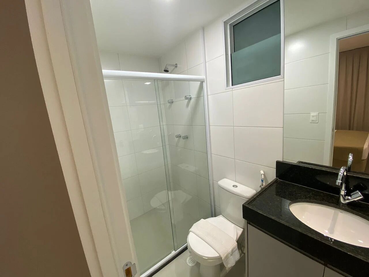 Un baño moderno con ducha de mampara de vidrio, inodoro blanco y lavamanos sobre encimera negra.
