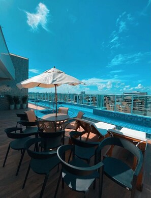 A rooftop pool area with lounge chairs and umbrellas, overlooking a cityscape. - Edifício Promenade II - Apto 403 (Maceio)