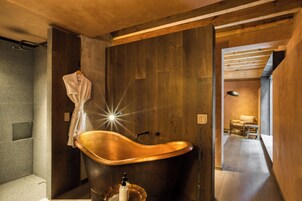 Un bagno moderno con una vasca freestanding, un portascopino e un pavimento in legno.
