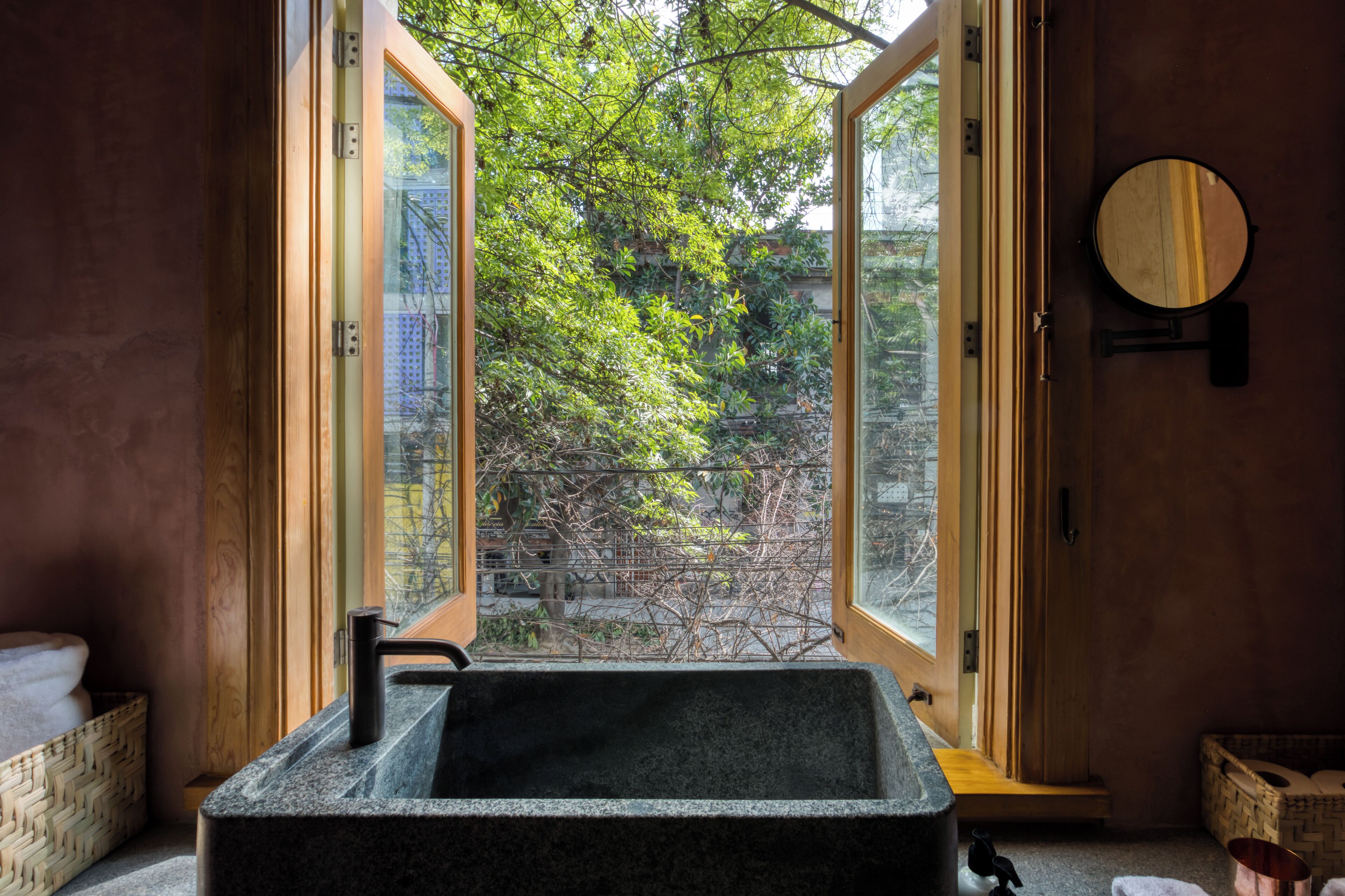 A bathroom with a stone sink, wooden door, and a view of greenery outside.