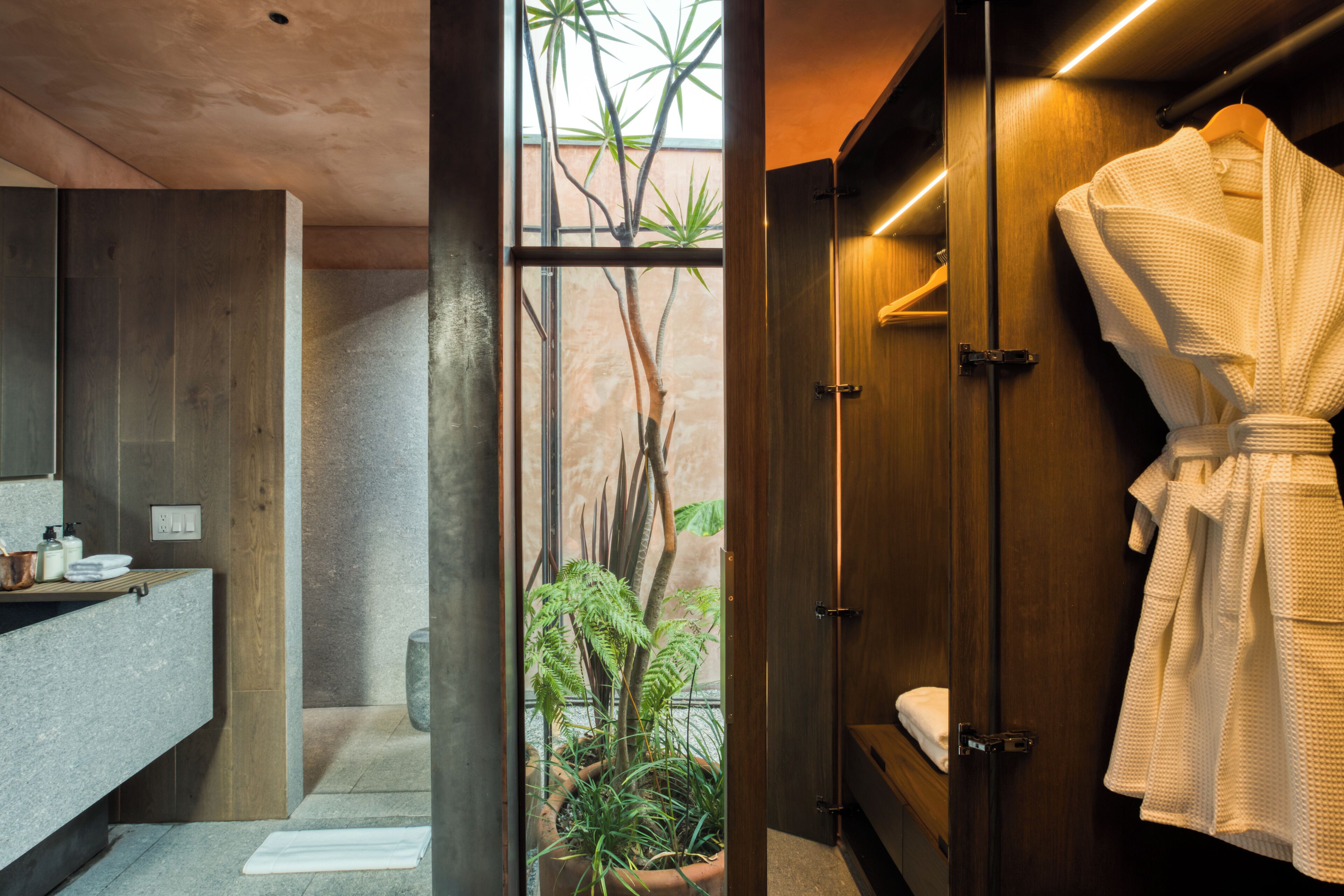 A modern bathroom with a wooden vanity, a large mirror, and a potted plant.
