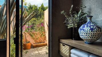 Quarto com uma grande janela com vista para um jardim, um vaso azul e branco numa estante, e uma cesta de vime.