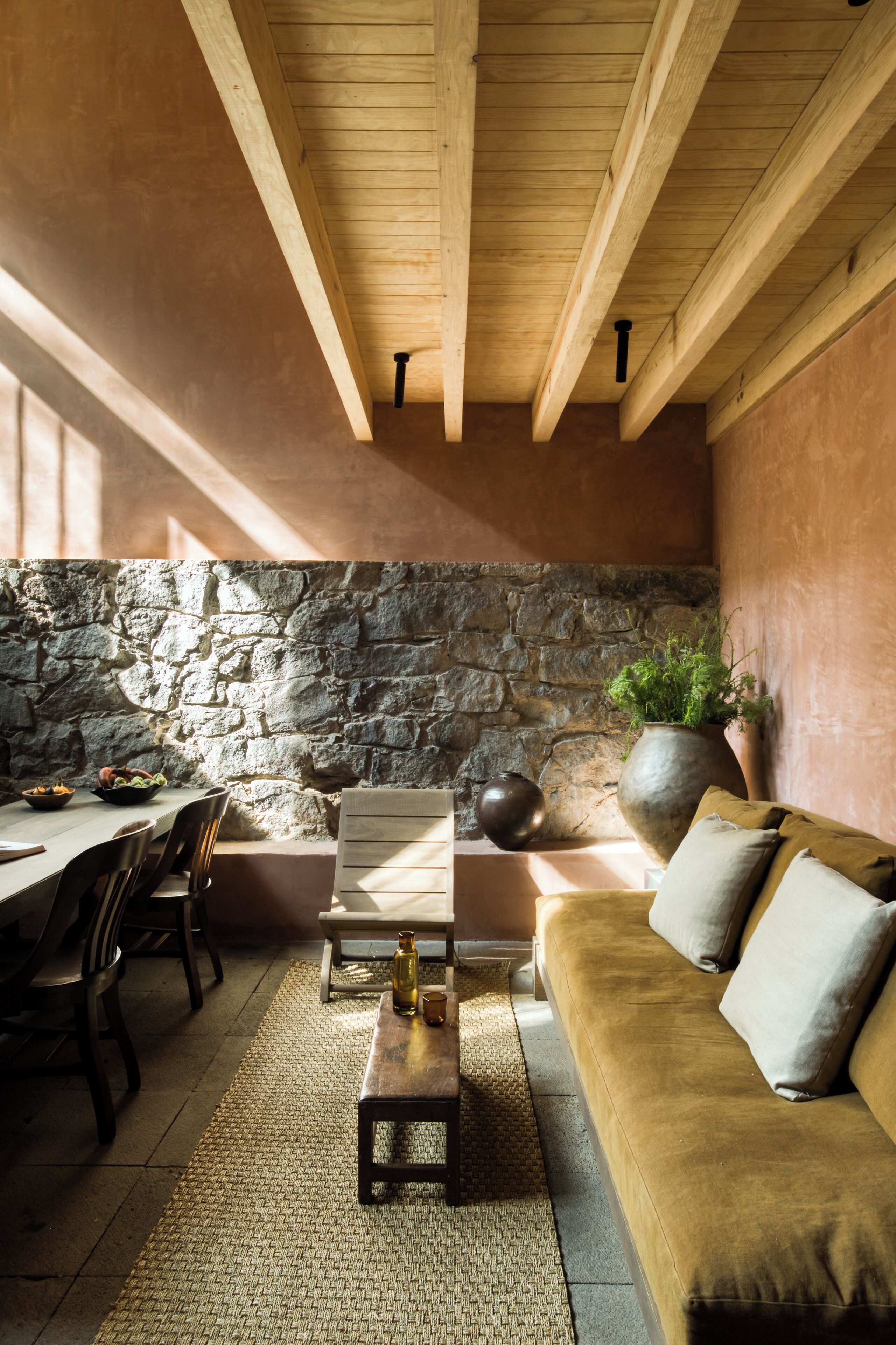 A cozy interior with a stone wall, wooden ceiling beams, a sofa, and a dining area.