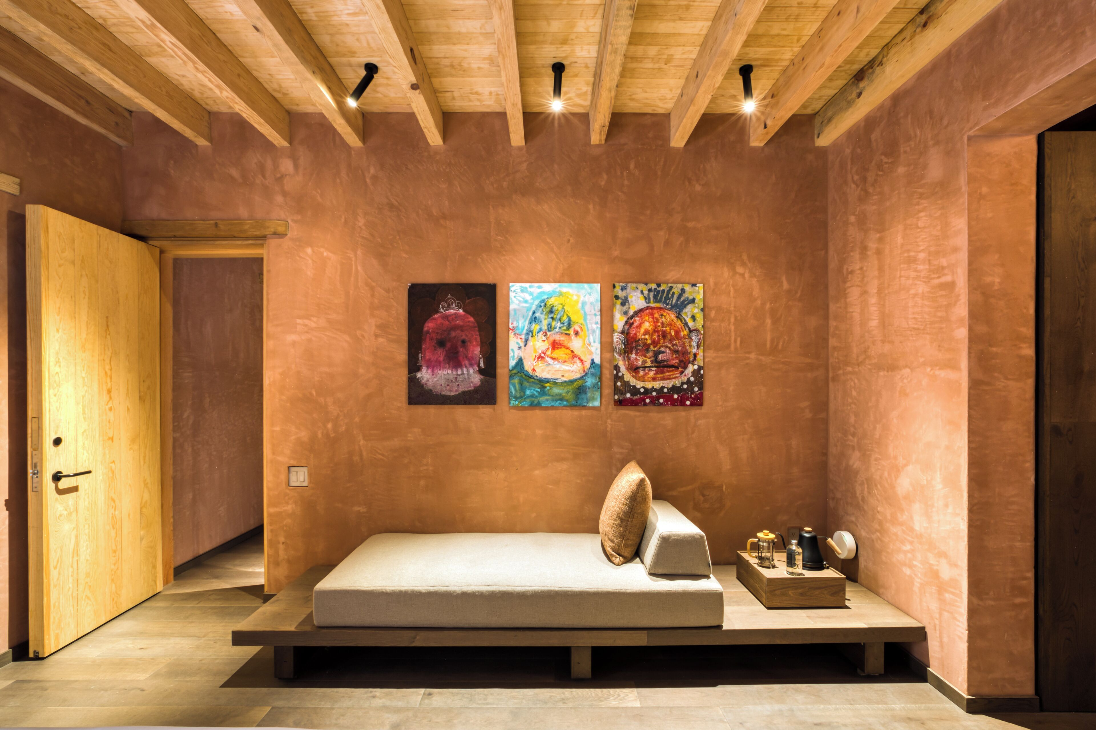 Una habitación con techo de madera, una cama con almohadas y tres cuadros en la pared.