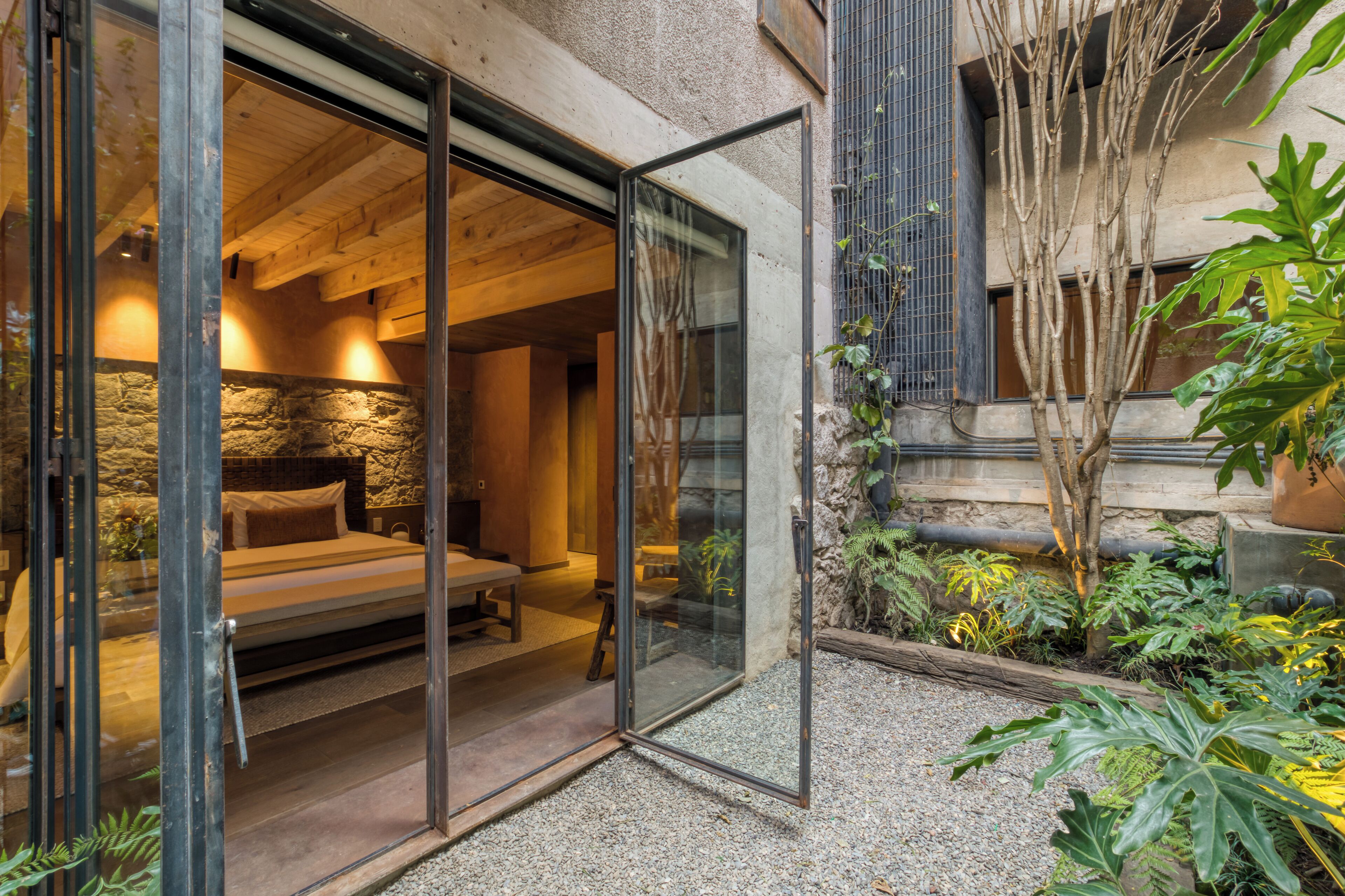 Une chambre moderne avec un mur en pierre, un lit et une porte vitrée donnant sur un jardin.