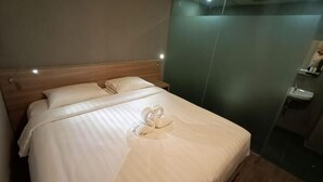 A hotel room with a bed, pillows, a towel, a mirror, and a sink. - Hotel Marina Airport (West Semarang)