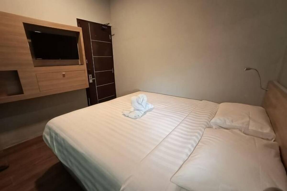 A neatly made bed with a folded towel, a wooden TV shelf, and a wardrobe.