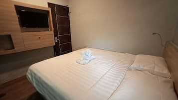 A neatly made bed with a folded towel, a wooden TV shelf, and a wardrobe.