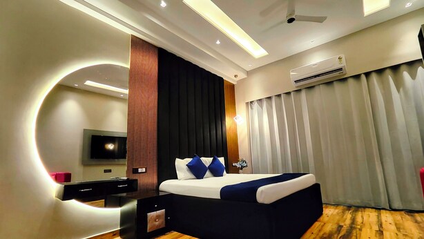 Une chambre d’hôtel moderne avec un plancher en bois, un lit avec une literie bleue et blanche, un miroir rond, un téléviseur à écran plat et un appareil de climatisation.