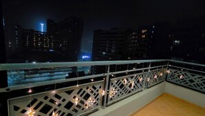 Un balcon doté d’une balustrade ornée de guirlandes lumineuses, offrant une vue sur le paysage urbain illuminé la nuit.