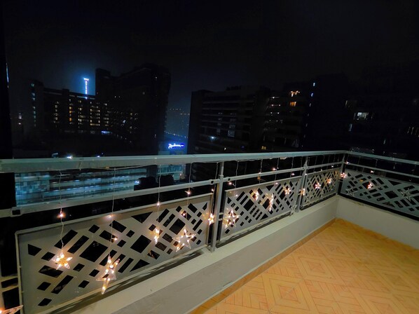 A balcony with a railing decorated with string lights, overlooking a cityscape at night. - The Spotlight (Greater Noida)