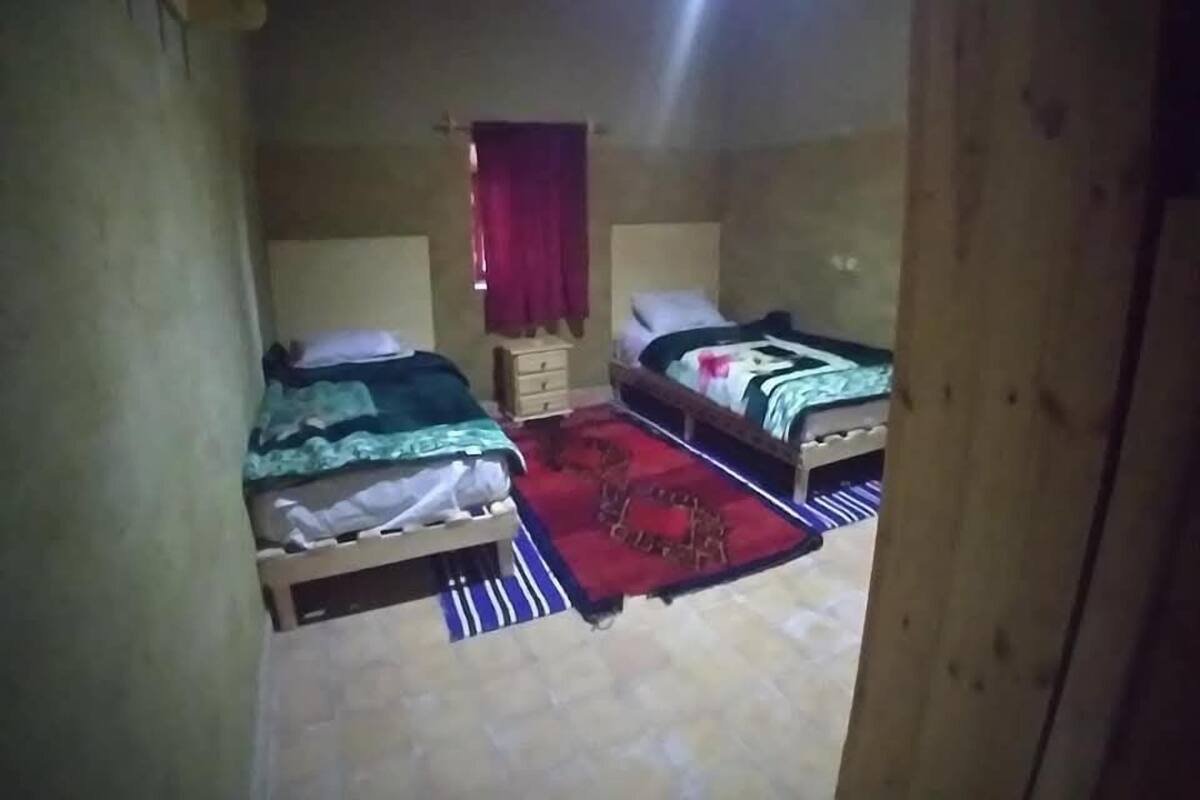 Une petite pièce étroite avec deux lits, une petite armoire en bois et un rideau rouge.