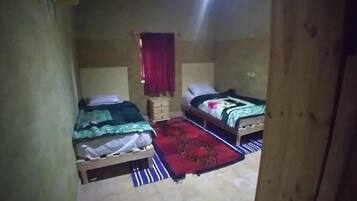 Una habitación estrecha con dos camas, un pequeño armario de madera y una cortina roja.