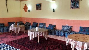 A room with a long sofa set, two round tables, patterned rugs, and wall-mounted lights. - Hôtel-Kasbah Aberdouz (Ait Yahya)