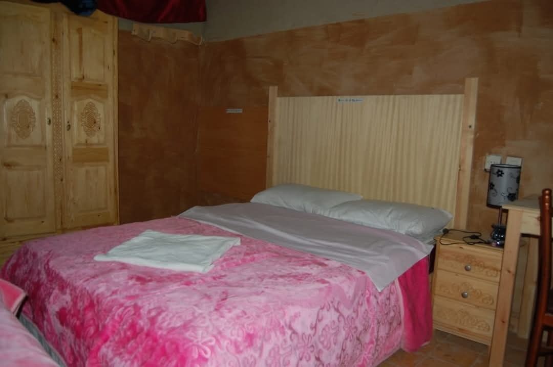 Une chambre à coucher comprenant un lit, une armoire en bois, une table de chevet avec une lampe et un petit bureau.