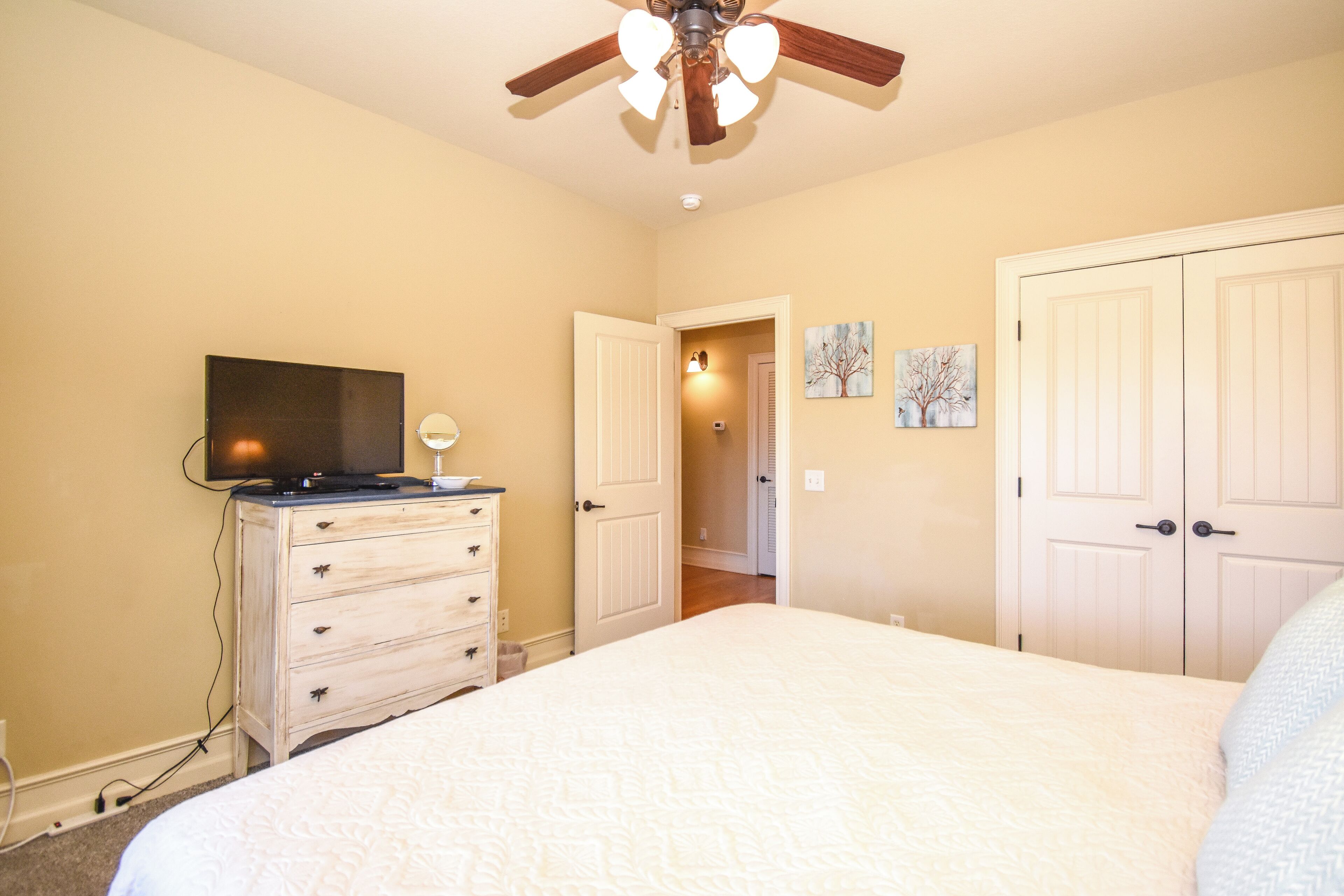 Une chambre à coucher comprenant un lit, une commode, un téléviseur et un ventilateur de plafond.