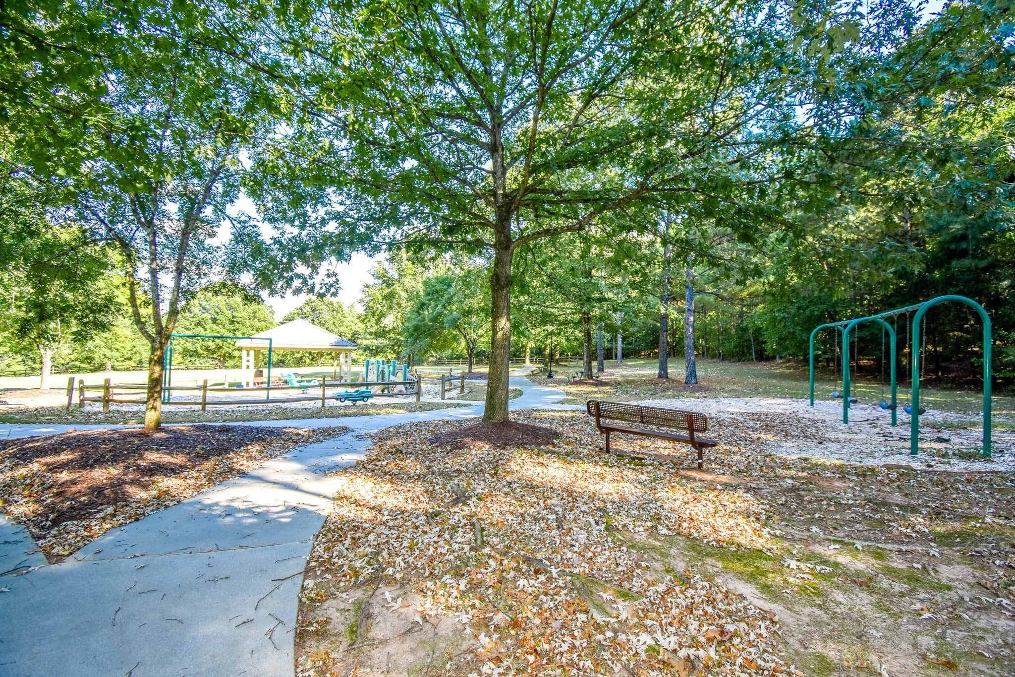 A park with a playground, a bench, and a covered pavilion.
