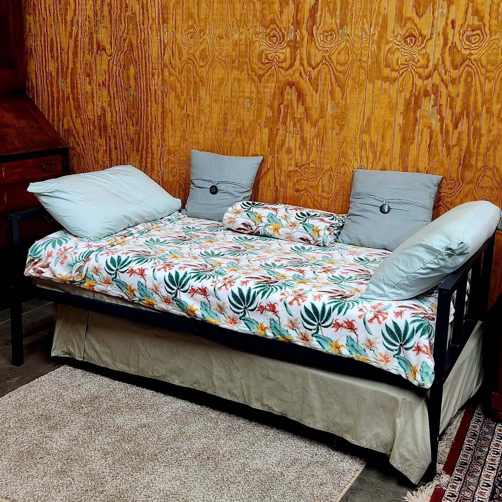Uma cama com colcha florida, duas almofadas e cabeceira de madeira.