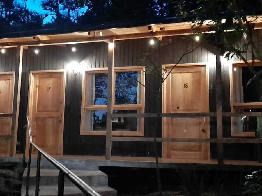 Eine Reihe aus Holzbungalows mit nummerierten Türen, jedes mit einem Fenster und einer kleinen Veranda.