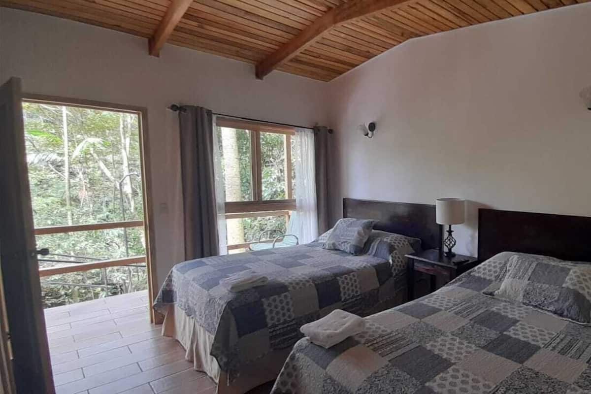 Un dormitorio con dos camas, techo de madera y un ventanal grande.