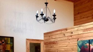 Zona pranzo in legno con tavolo e sedie, un lampadario e una parete in legno decorata con un quadro.