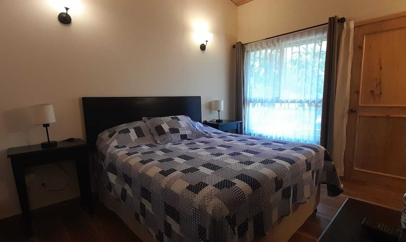 A bedroom with a bed, two bedside tables, a nightstand, a window with curtains, and a door.
