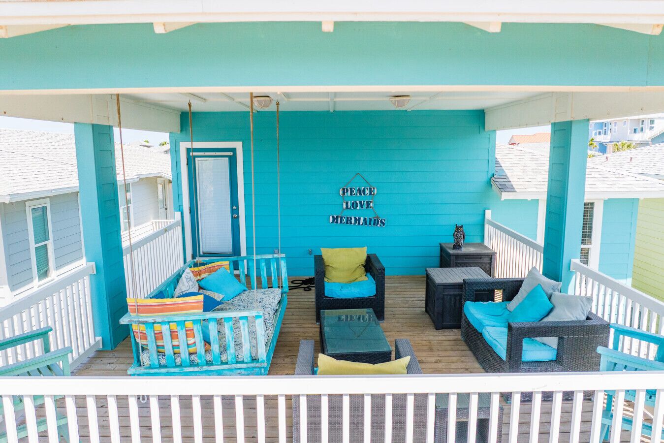 Una terraza turquesa con barandilla blanca, una puerta azul y un letrero que dice 'Peace Love Mermaids'.