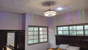 Ein Schlafzimmer mit Bett, zwei Fenstern, einer Deckenleuchte und einer Tür.