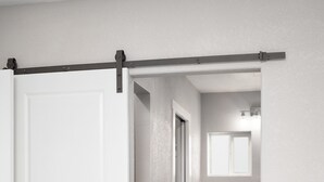 A hallway with a white door, a wooden floor, and a bathroom with a sink and mirror.