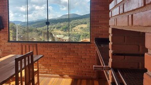 A room with a large window overlooking a mountainous landscape, a wooden table, and a brick fireplace. - Villa da Serra Ibitipoca (Lima Duarte)