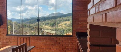 Ein Zimmer mit einem großen Fenster mit Blick auf eine gebirgige Landschaft, einem Holztisch und einem Kamin aus Backstein.