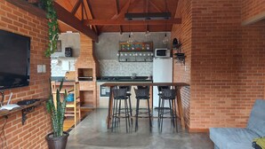 A compact kitchen with a brick wall, a built-in microwave, and a bar area with stools. - Villa da Serra Ibitipoca (Lima Duarte)