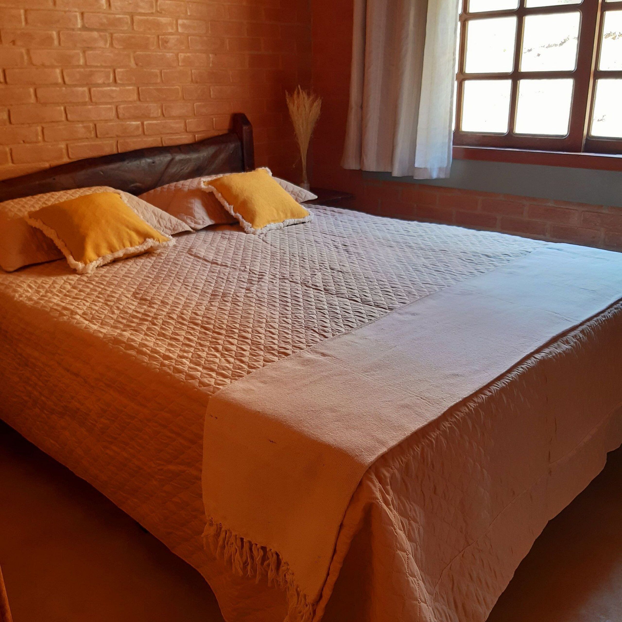 A bed with a quilted cover and two pillows, a brick wall, and a window with curtains.
