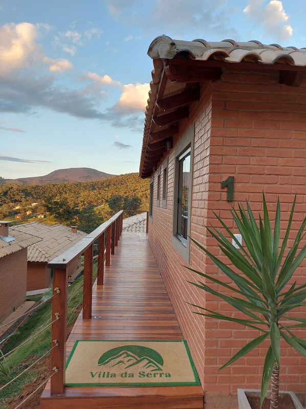 A wooden deck leading to a brick building with a mountain view. - Villa da Serra Ibitipoca (Lima Duarte)
