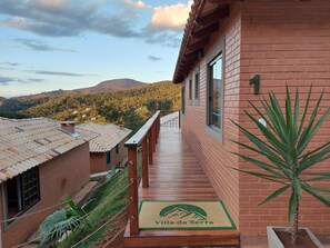 A wooden deck leading to a brick building with a mountain view. - Villa da Serra Ibitipoca (Lima Duarte)