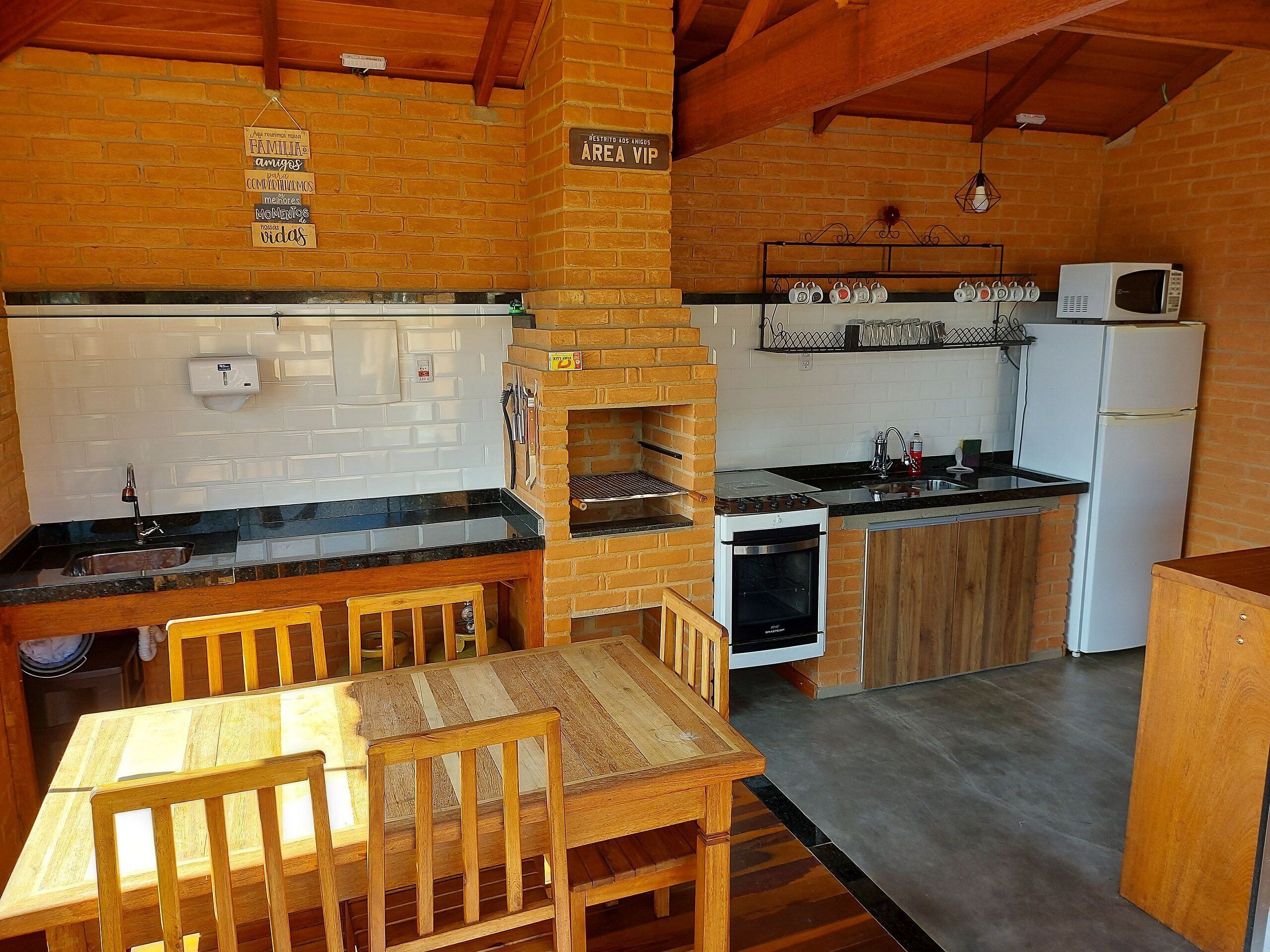 A kitchen with a brick wall, wooden table, chairs, a stove, oven, microwave, and a refrigerator.