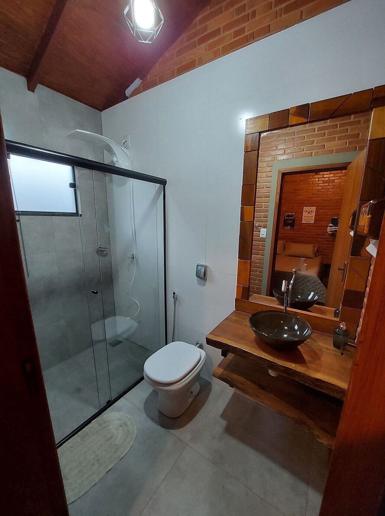 Un bagno con doccia vetrata, un WC bianco e un mobile bagno in legno con lavandino nero.