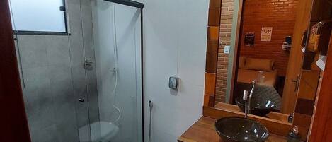 Un bagno con doccia vetrata, un WC bianco e un mobile bagno in legno con lavandino nero.