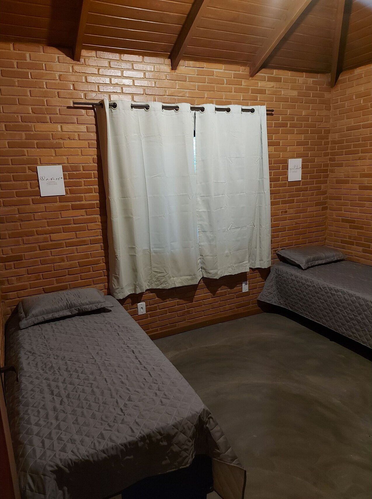 Quarto com duas camas, parede de tijolos e teto de madeira.