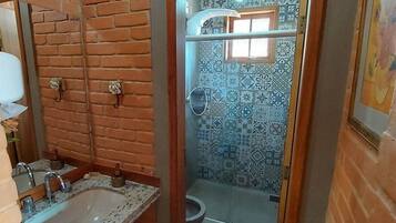 Un baño con pared de ladrillo, un lavabo con espejo y una zona de ducha con azulejos estampados.