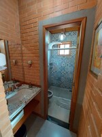 Un baño con pared de ladrillo, un lavabo con espejo y una zona de ducha con azulejos estampados.