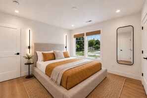 A modern bedroom with a bed, bedside tables, a large mirror, and a view of the outdoors.