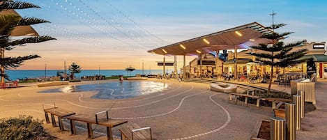 Un passeig marítim amb una zona coberta per seure, una piscina i un restaurant.